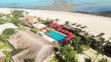 Un complexe hôtelier doté d’une piscine, d’un accès à la plage et de bâtiments à toits de chaume.