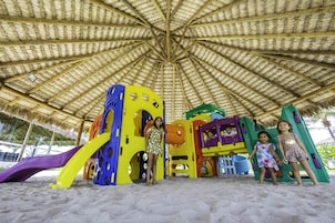 Uma área de recreação na praia com um telhado de palha e estruturas coloridas.