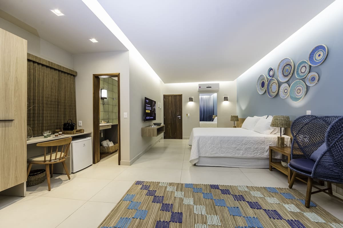 A modern hotel room with a bed, desk, chair, TV, and decorative wall art.
