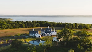 Une grande maison à étages, dotée d’une architecture symétrique, entourée d’une pelouse bien entretenue et d’un petit étang.