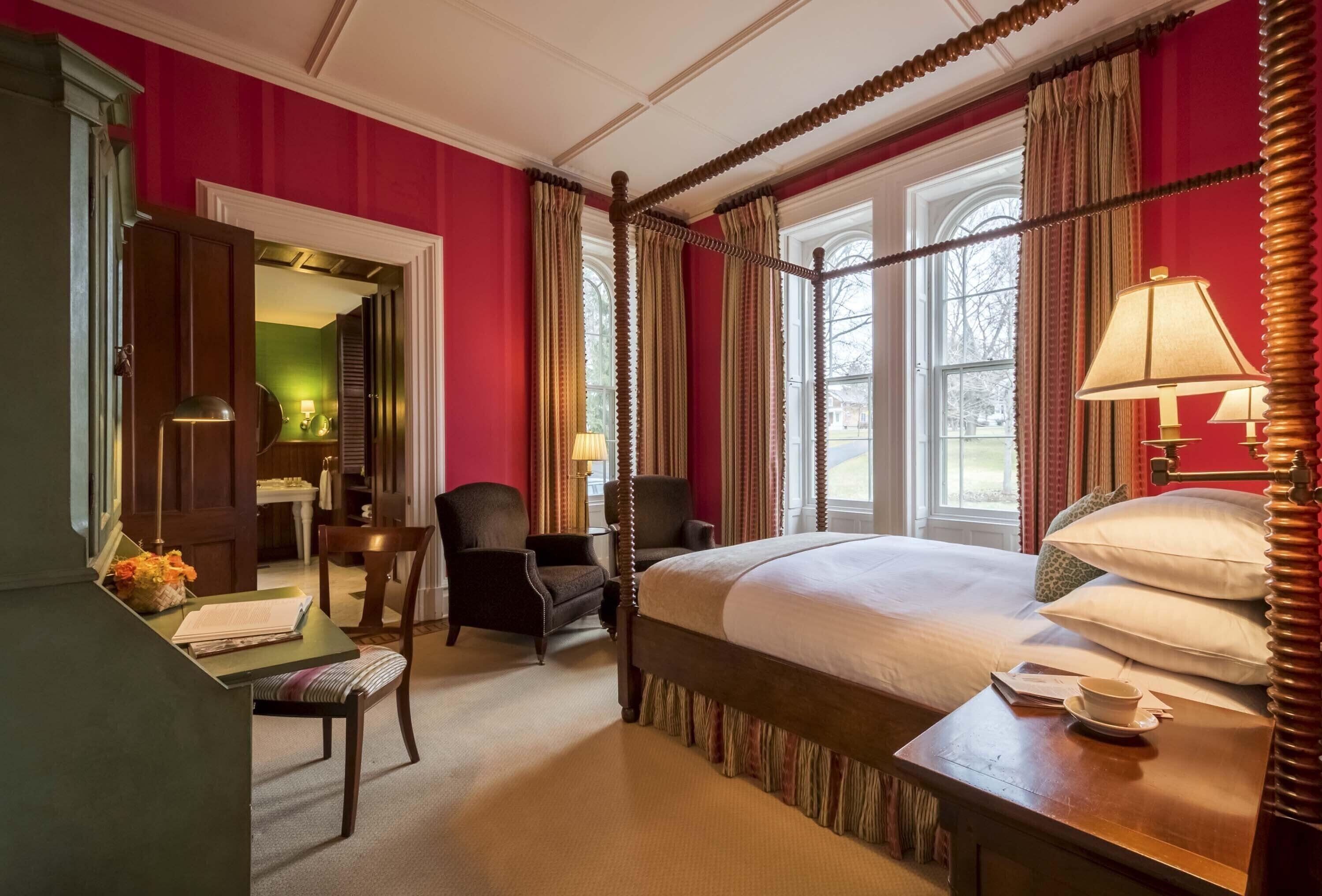A four-poster bed with a canopy, a desk with a chair, and a window with curtains.