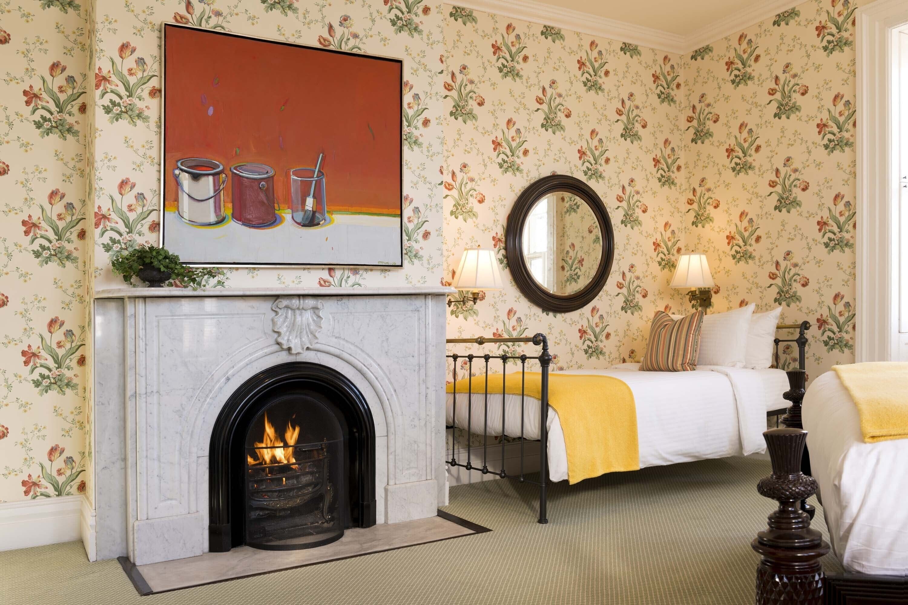 A room with a fireplace, a bed, a bedside table, and a mirror.
