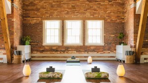 Une pièce avec un mur en briques, trois fenêtres, un plancher en bois et un espace central dédié à la pratique du yoga.