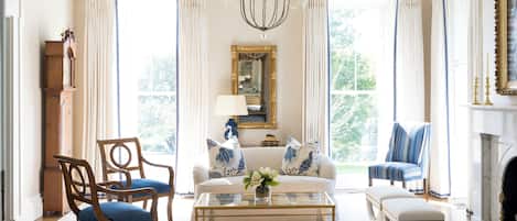 A spacious living room with a chandelier, a fireplace, and a large window with curtains.