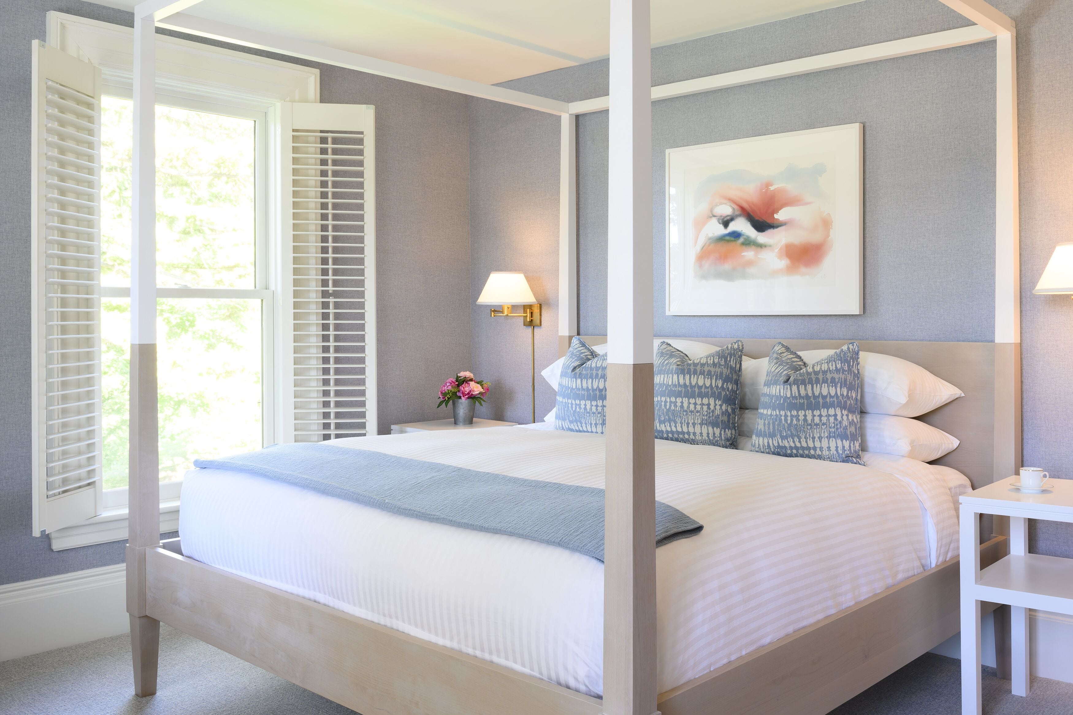 Uma cama com dossel, um criado-mudo com abajur e um quadro na parede.