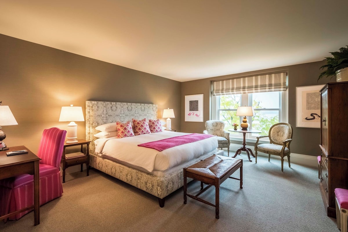 A hotel room with a large bed, two bedside tables with lamps, a chair, a small table, and a cabinet.