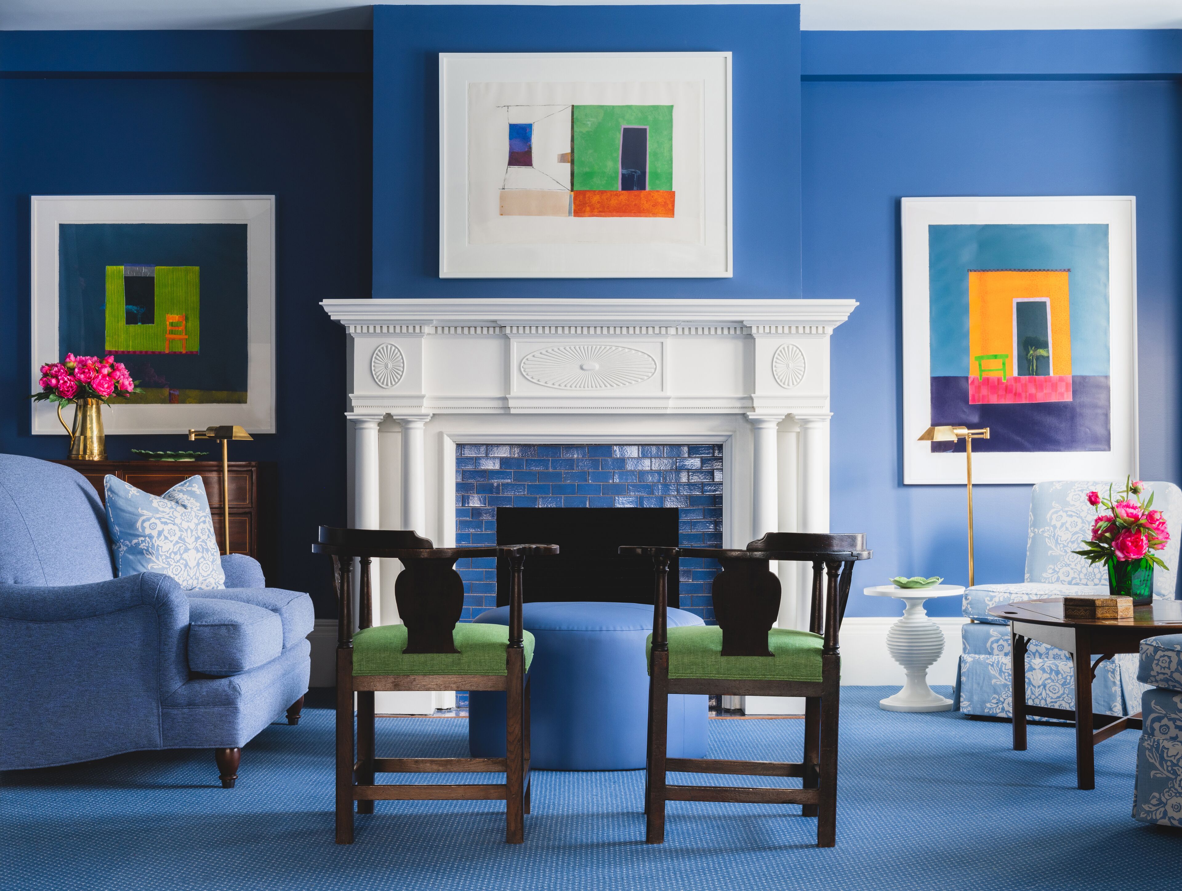 A living room with a blue sofa, two wooden chairs, a fireplace, and artwork on the walls.