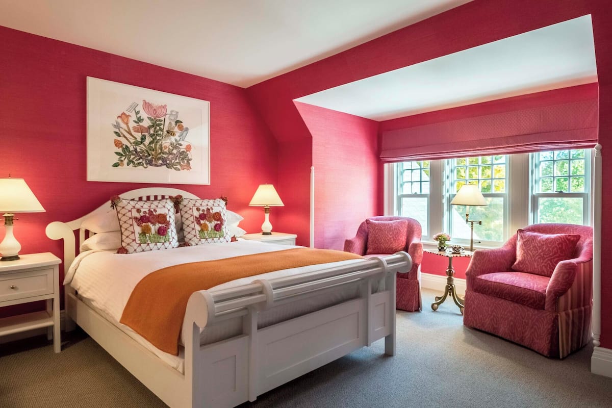 A bedroom with a white bed, red walls, and a large window.