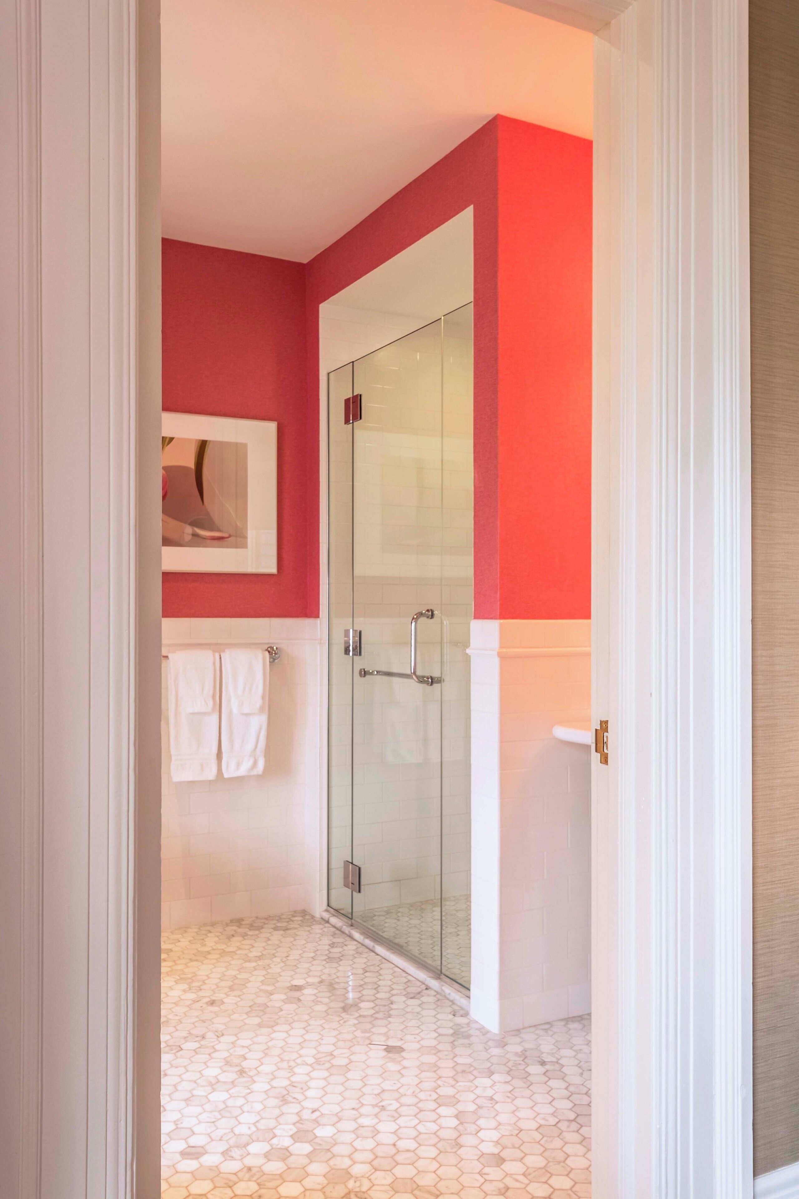 A bathroom with a glass shower enclosure, white tiled floor, and red walls.