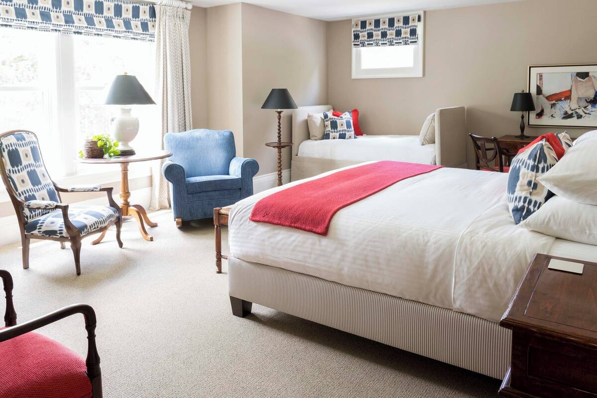 A hotel room with a large bed, two chairs, a small table, and a desk.