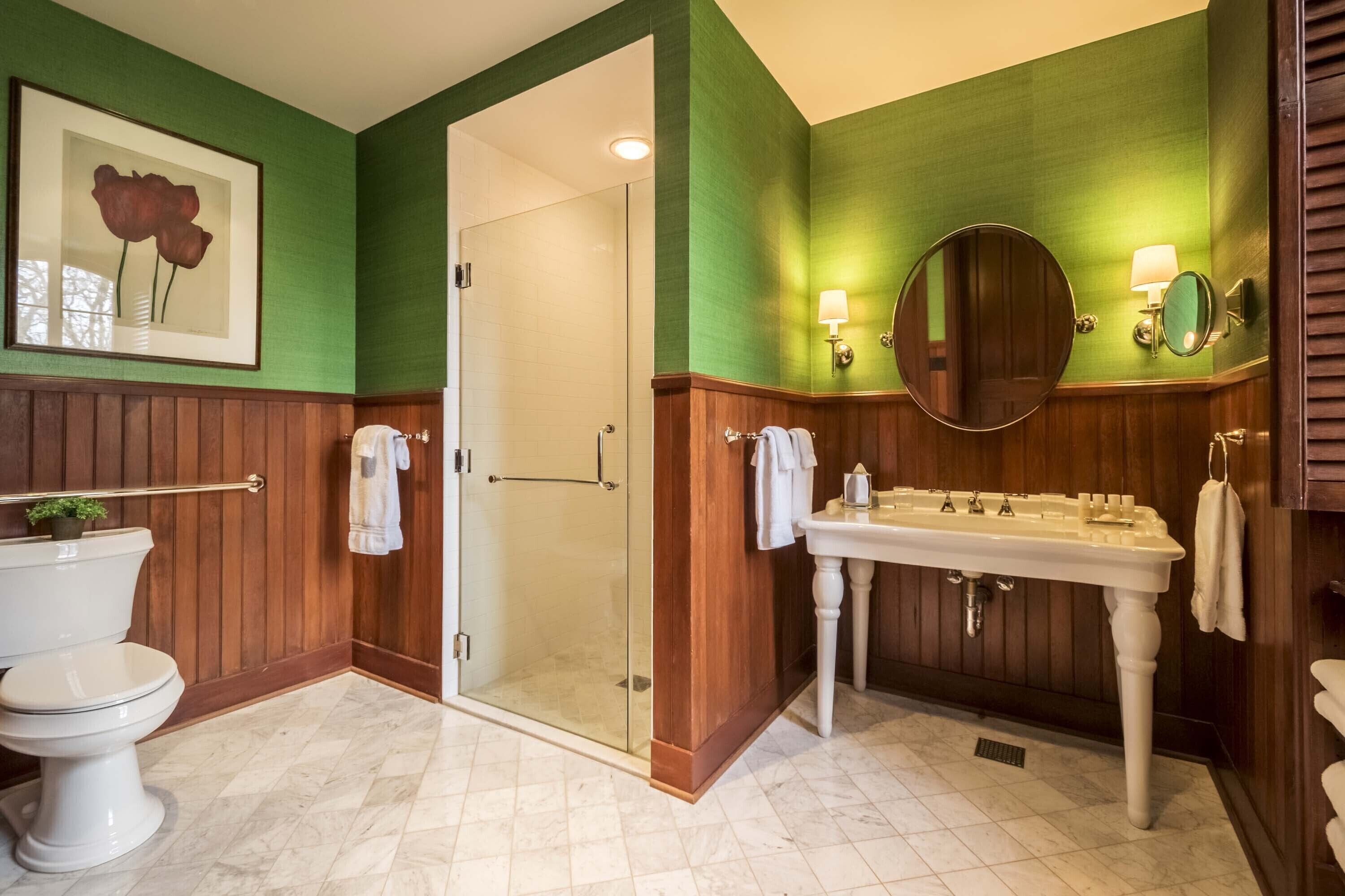 A bathroom with a glass shower enclosure, a white sink with a mirror, and a framed picture on the wall.