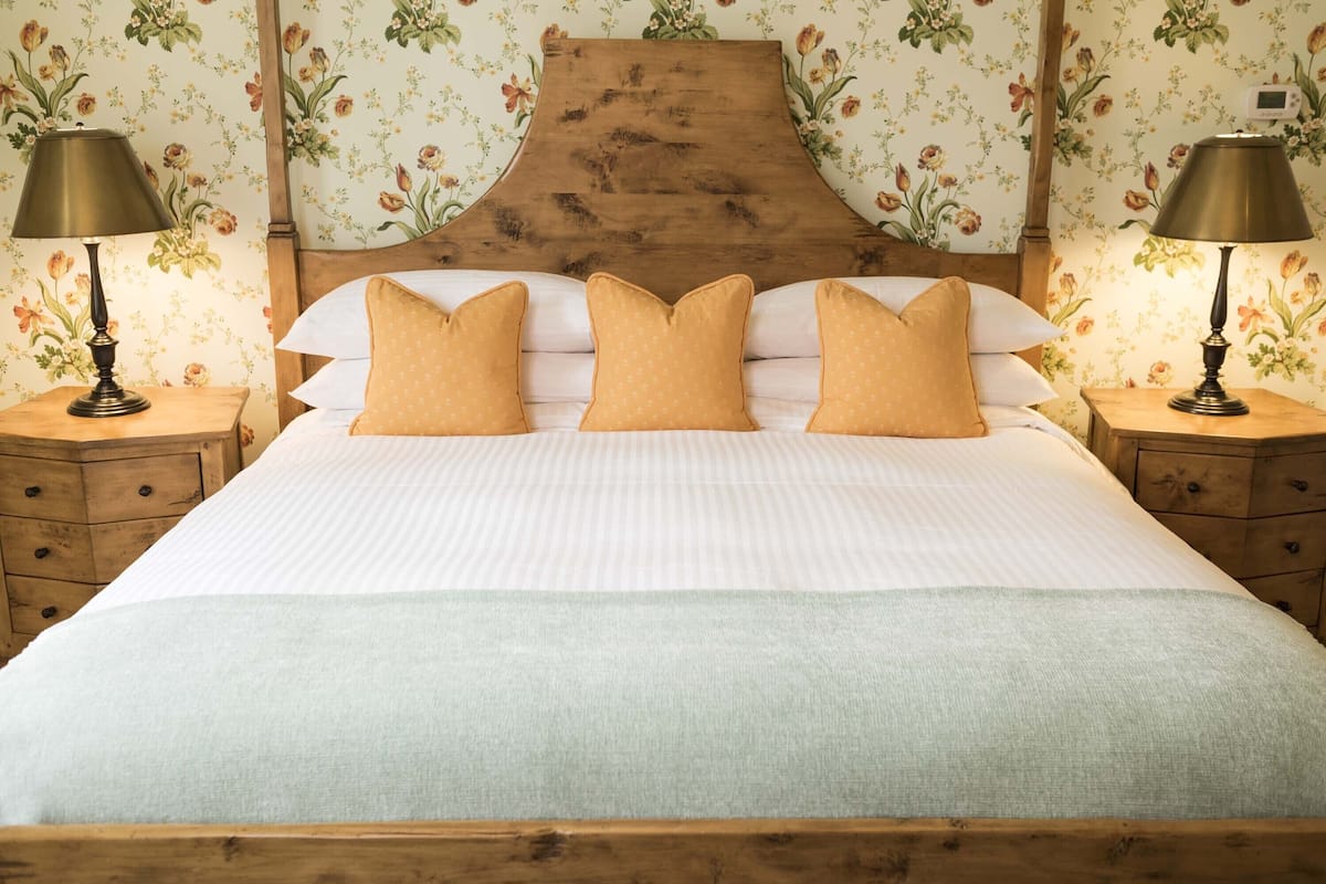 A neatly made bed with a wooden headboard, two bedside tables with lamps, and floral wallpaper.