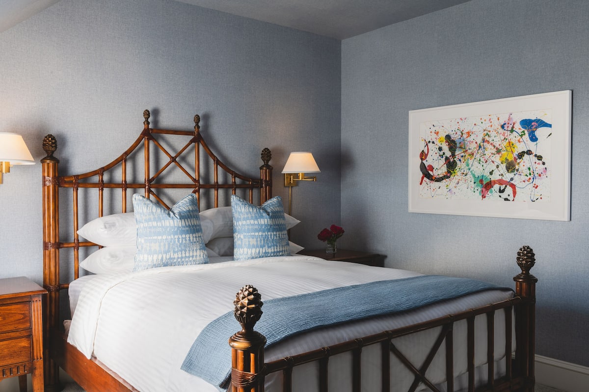 A neatly made bed with a wooden headboard, two bedside lamps, and a framed abstract painting on the wall.