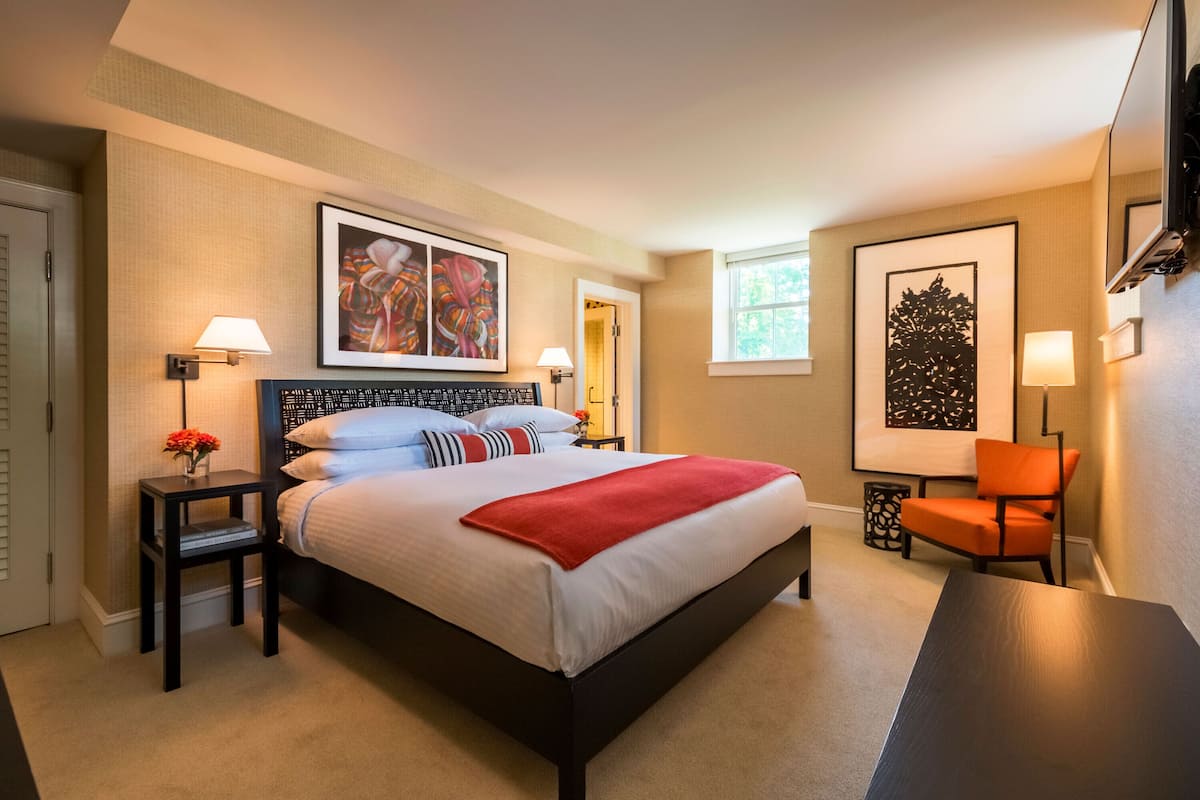 A neatly arranged hotel room with a large bed, two bedside tables with lamps, a chair, and artwork on the walls.