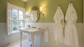 A bathroom with a white sink, two white robes hanging on the wall, and a window with shutters.