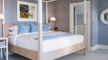 A neatly arranged bedroom with a four-poster bed, a bedside table with a lamp, and a framed artwork on the wall.