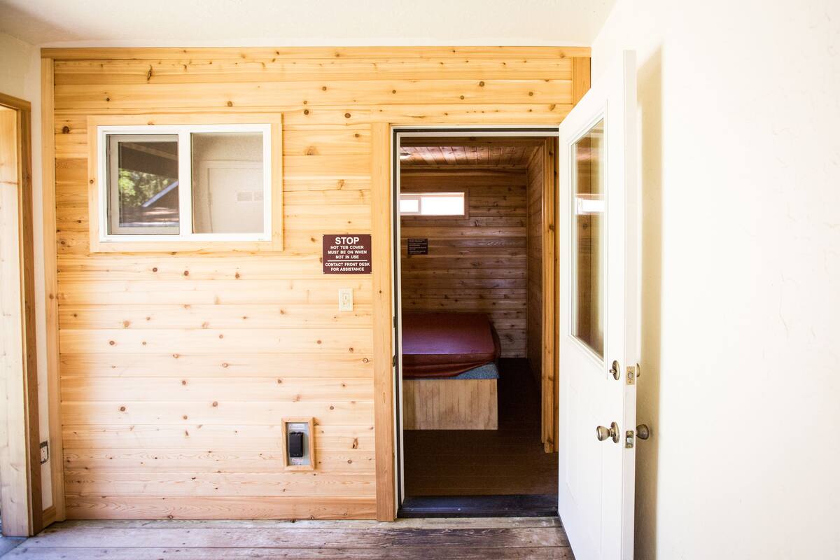 A wooden cabin interior with a single bed, a window, and a door.