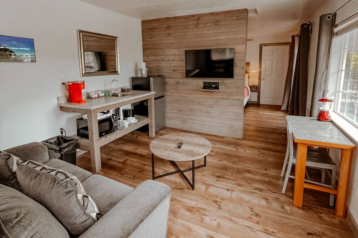 A modern living room with a grey sofa, a wooden coffee table, and a TV mounted on a wooden wall.