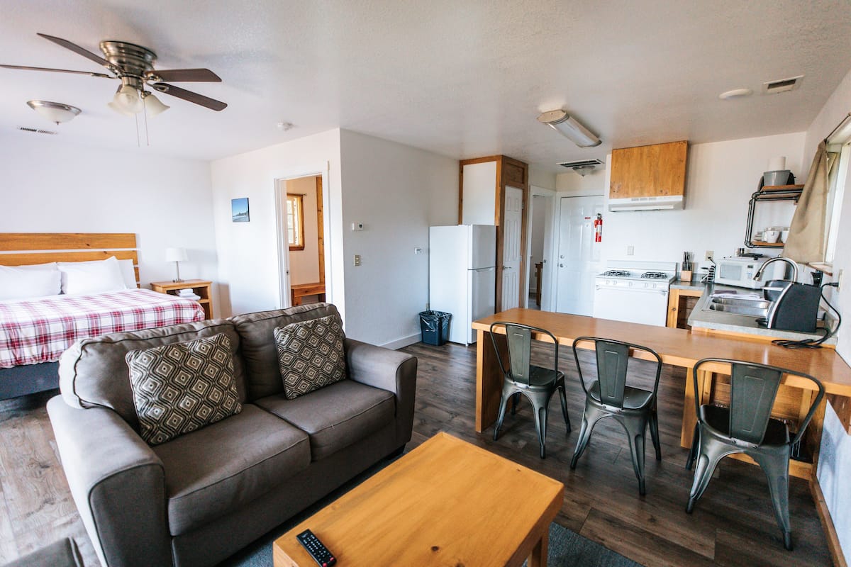A compact hotel room with a kitchenette, a dining area, and a living space with a sofa and a coffee table.