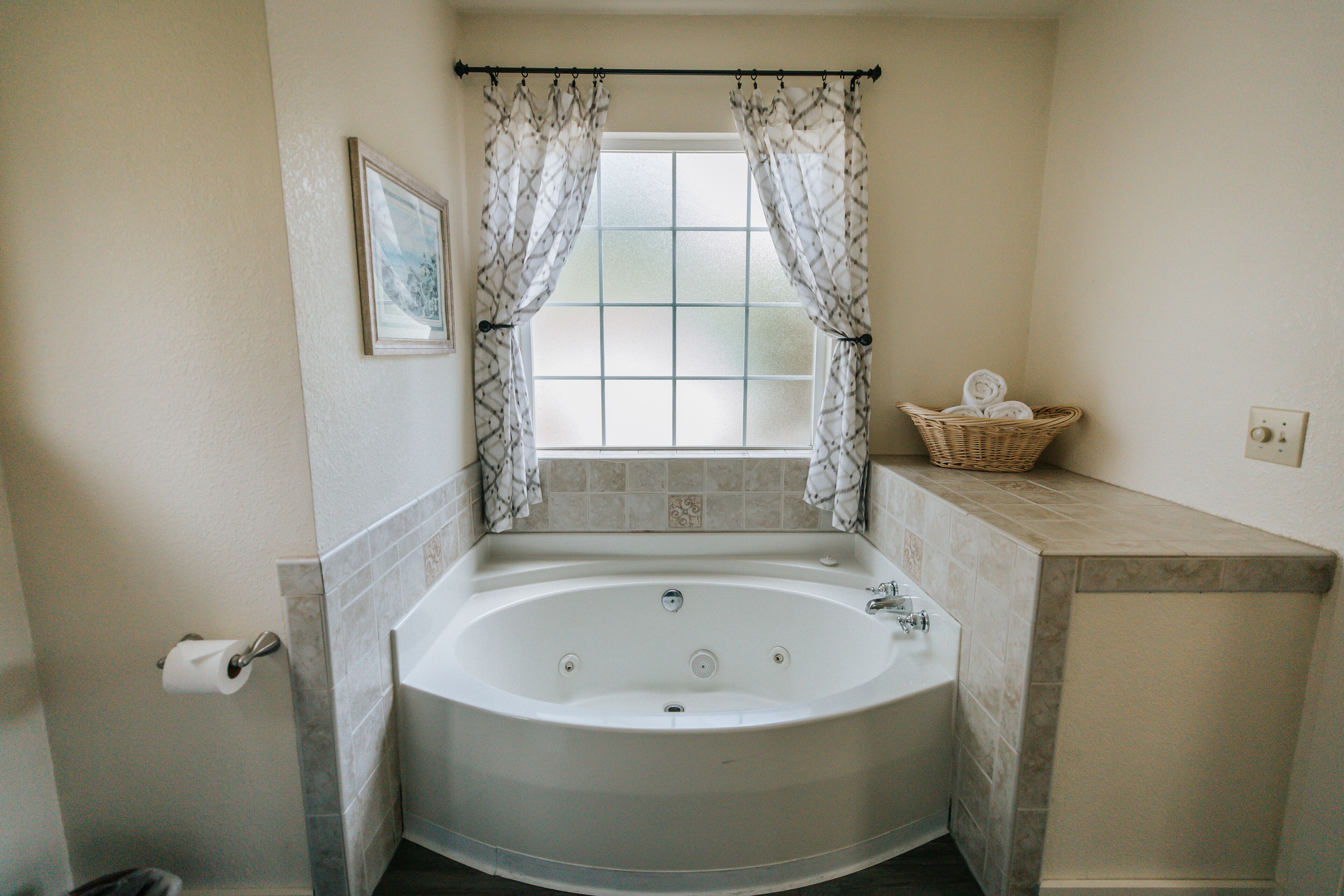 A bathroom with a freestanding bathtub, a window with curtains, a towel rack, and a basket on the countertop.