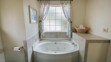 A bathroom with a freestanding bathtub, a window with curtains, a towel rack, and a basket on the countertop.