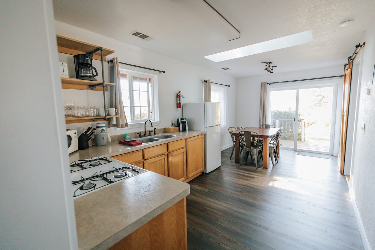 A kitchen with wooden cabinets, a gas stove, a sink, and a refrigerator. There is a dining area with a table and chairs.
