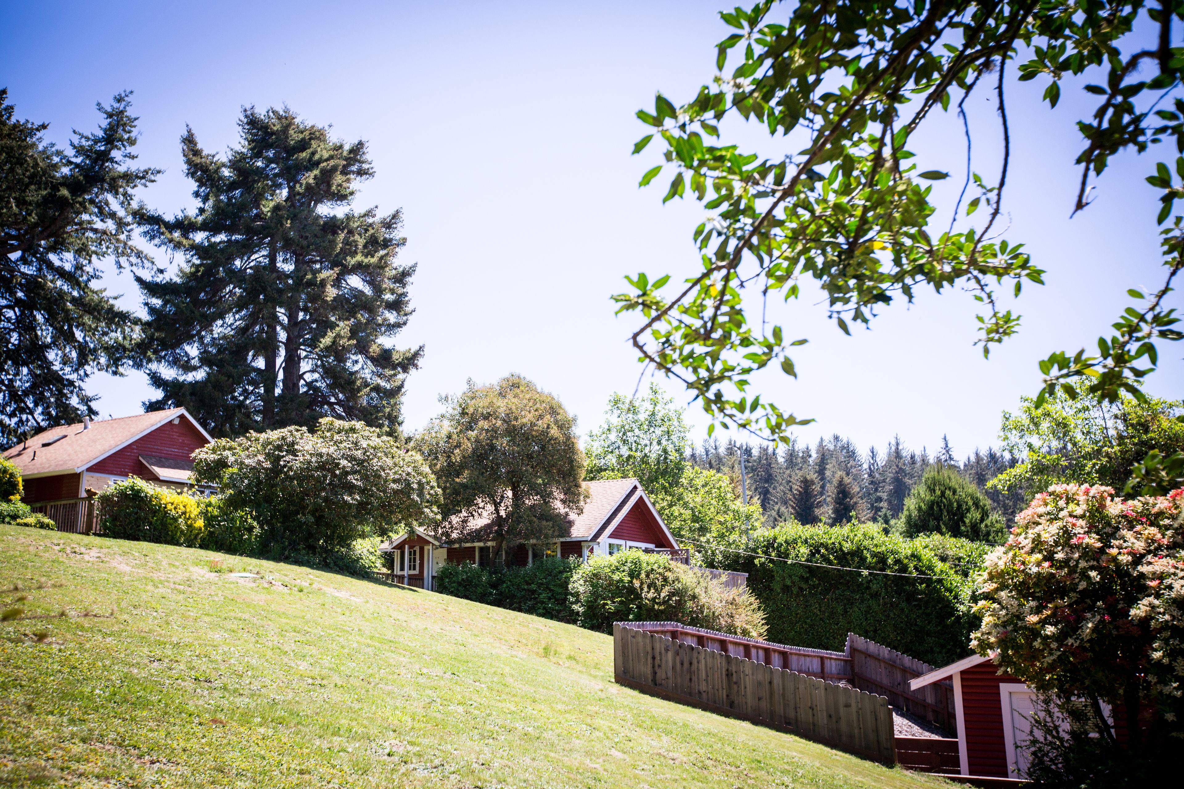 A residential area with a grassy slope, a wooden fence, and a red building with a sloped roof.