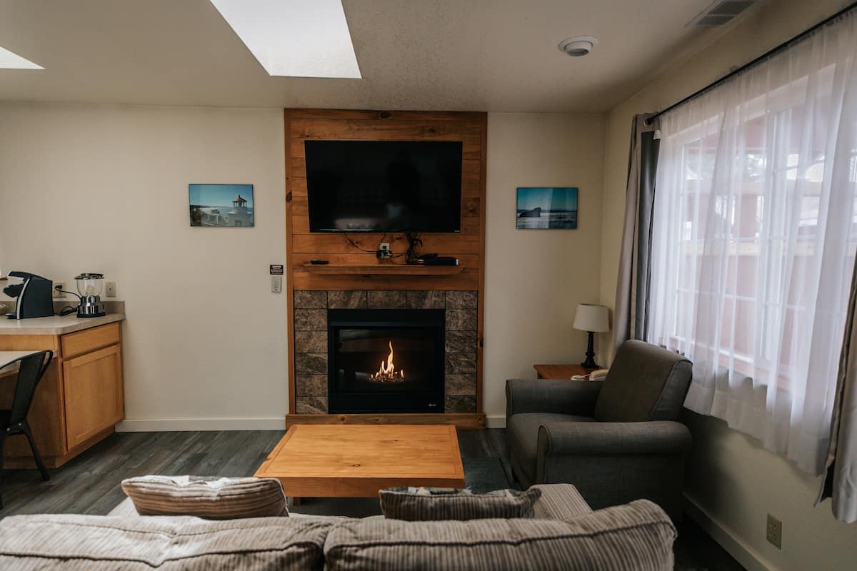 A living room with a fireplace, a television mounted on the wall, a sofa, a coffee table, and a dining area with a chair and a table.