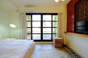 Ein Hotelzimmer mit Bett, Fernseher, Fenster mit Vorhängen und einer Ziegelwand.