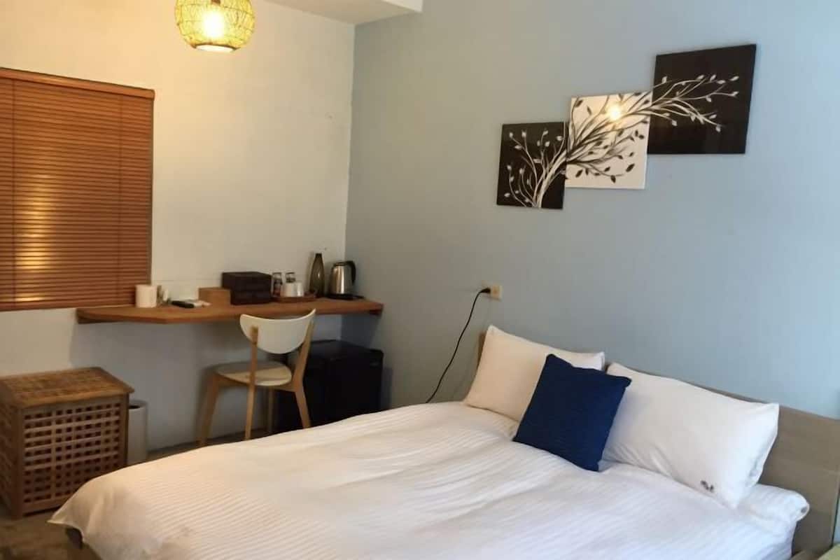 A bedroom with a bed, a desk, a chair, and a wall-mounted light fixture.