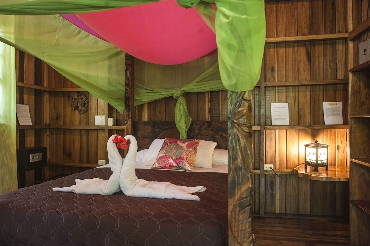 Une pièce en bois avec un lit, un baldaquin vert et une table de chevet avec une lampe.