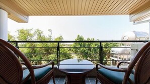 A balcony with wicker chairs and a glass table, overlooking a green landscape and a barbecue grill. - Coconut Grove House B and B (Hengchun)