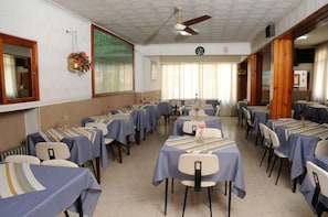 A dining hall with multiple tables and chairs, a ceiling fan, and a clock on the wall. - Hotel Florida (Villa Carlos Paz)