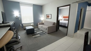 A hotel room with a desk, office chair, sofa, and a bed. - Home2 Suites by Hilton Tulsa Hills (Tulsa)