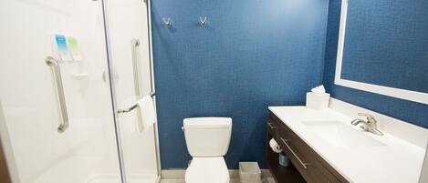A bathroom with a white toilet, a glass shower enclosure, a blue tiled wall, and a white sink with a mirror.