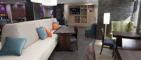 A modern hotel lobby with a seating area, a TV, and a bar.
