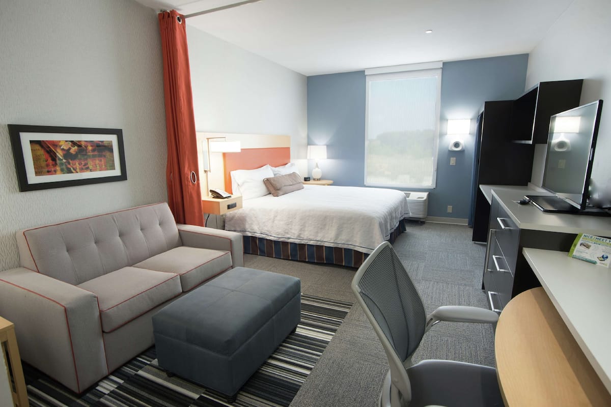 A hotel room with a bed, a sofa, a desk, and a TV.
