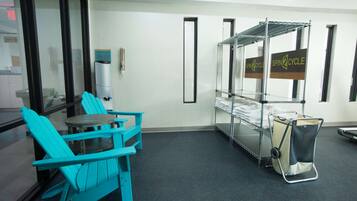 A room with a teal chair, a small round table, a metal rack with folded towels, and a bag on a stand.