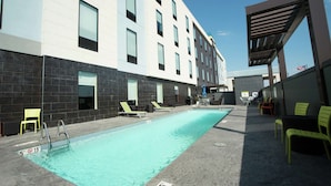 A modern building with a swimming pool, lounge chairs, and a covered seating area. - Home2 Suites by Hilton Tulsa Hills (Tulsa)