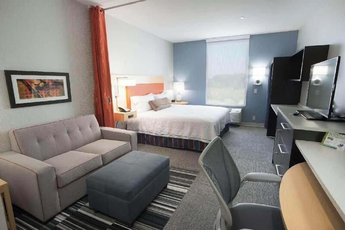 A hotel room with a bed, a sofa, a desk, a chair, a television, and a painting on the wall.
