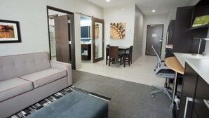 A modern hotel room with a sofa, a desk, and a dining area. - Home2 Suites by Hilton Tulsa Hills (Tulsa)
