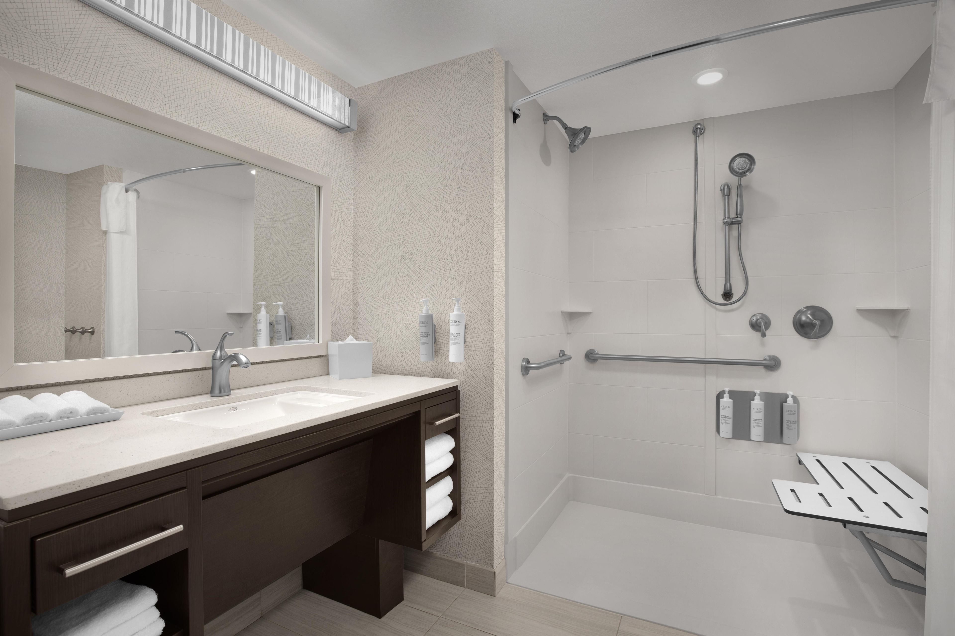 Une salle de bain moderne dotée d’un grand miroir, de deux vasques, d’une douche avec un pommeau de douche amovible et d’un espace de douche clos par des parois de verre.