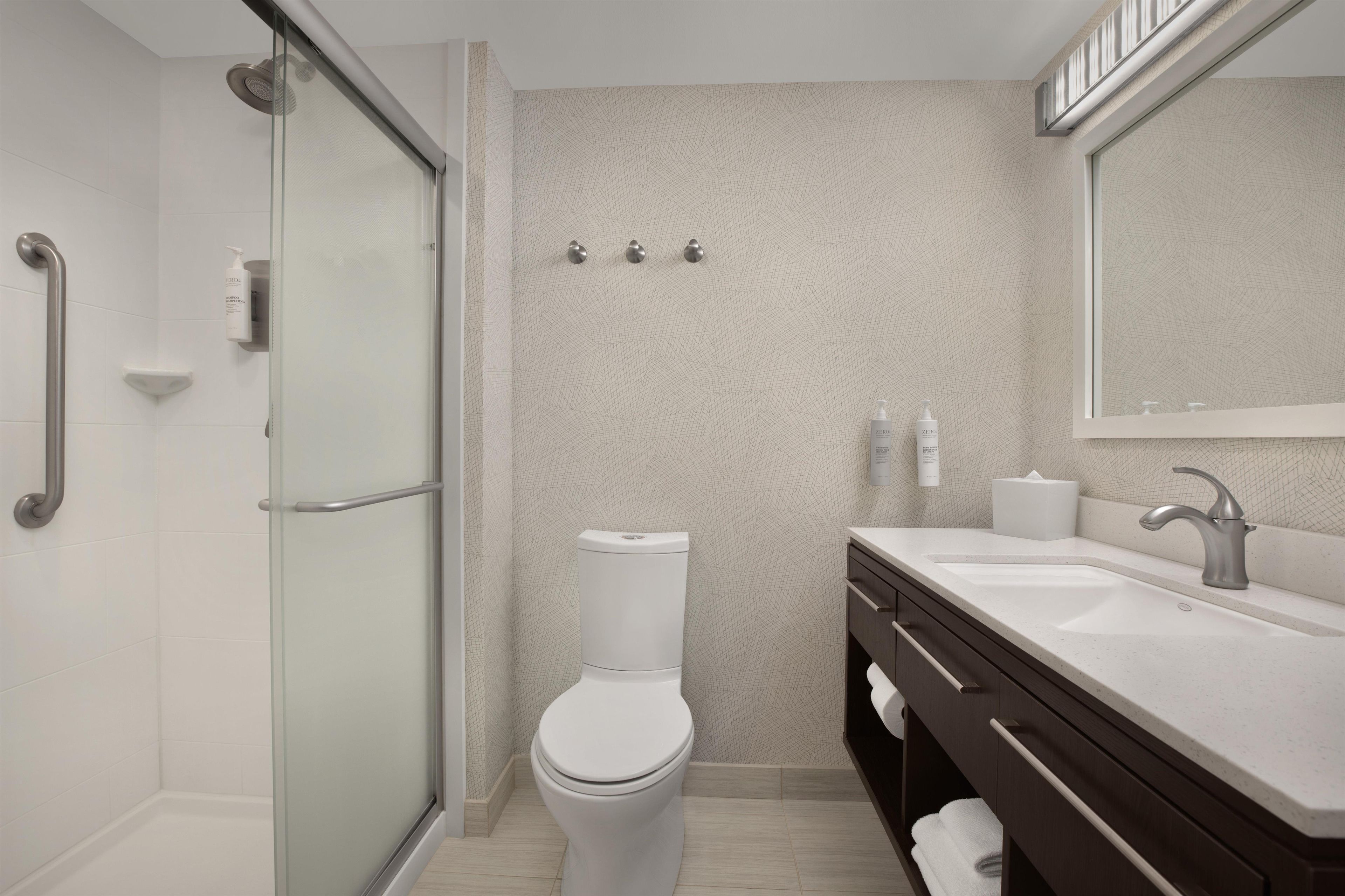 Une salle de bain moderne avec une douche à parois de verre, des toilettes blanches, un lavabo avec un meuble-vasque foncé et un grand miroir.