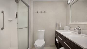 Une salle de bain moderne avec une douche à parois de verre, des toilettes blanches, un lavabo avec un meuble-vasque foncé et un grand miroir.