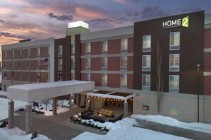 A hotel with a covered outdoor seating area, multiple windows, and an American flag. - Home2 Suites by Hilton Anchorage / Midtown (Anchorage)