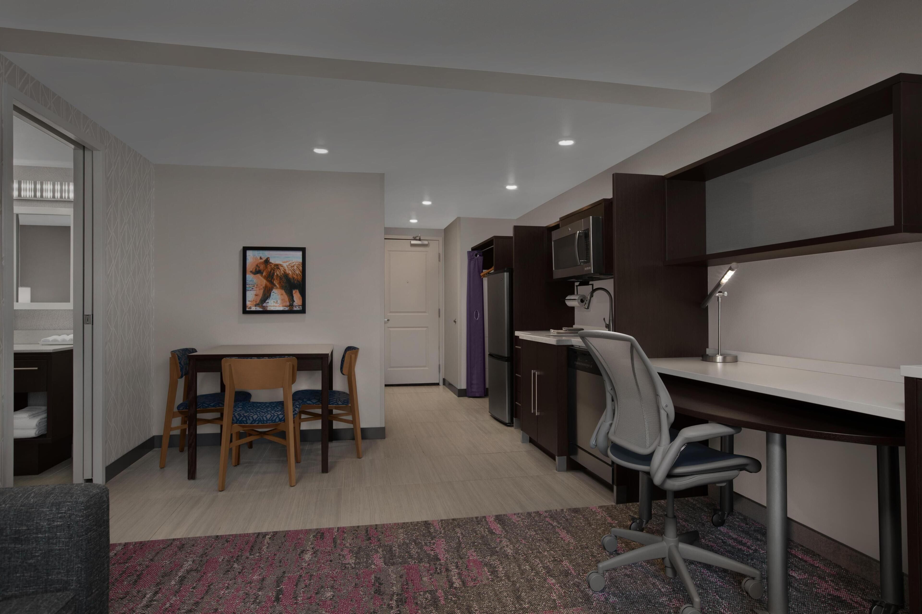 A modern kitchen with a dining area, a microwave, a refrigerator, and a desk with a chair.