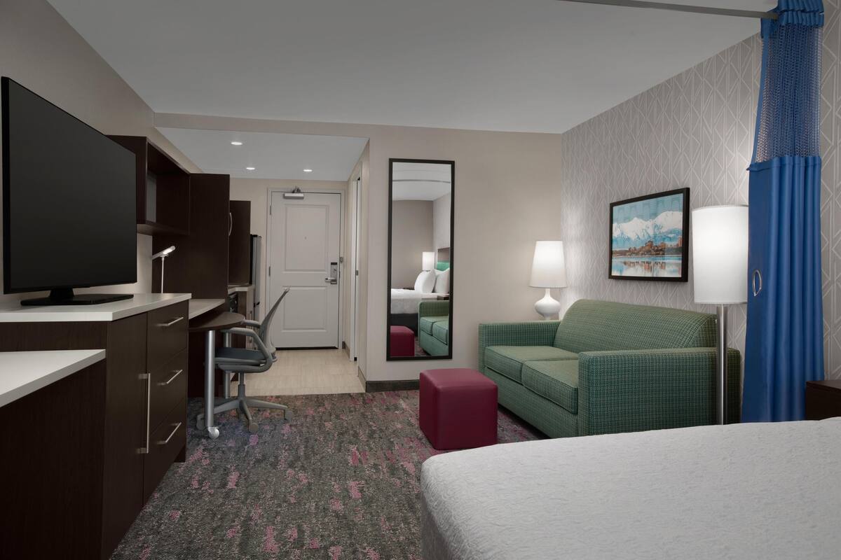 A hotel room with a bed, desk, chair, television, and a mirror.