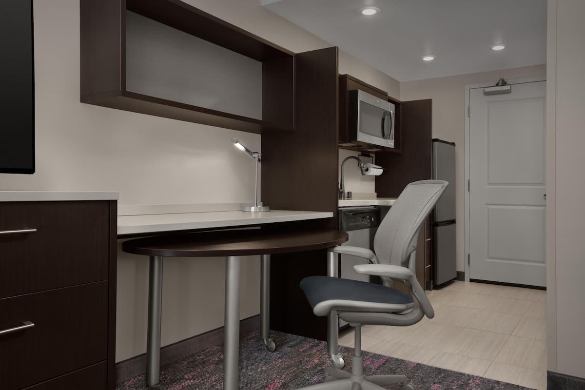 A modern kitchen with a built-in microwave, a refrigerator, a dining table, and a chair.
