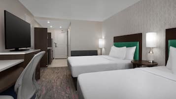 A hotel room with a desk, two beds, a TV, and a bathroom in the background.