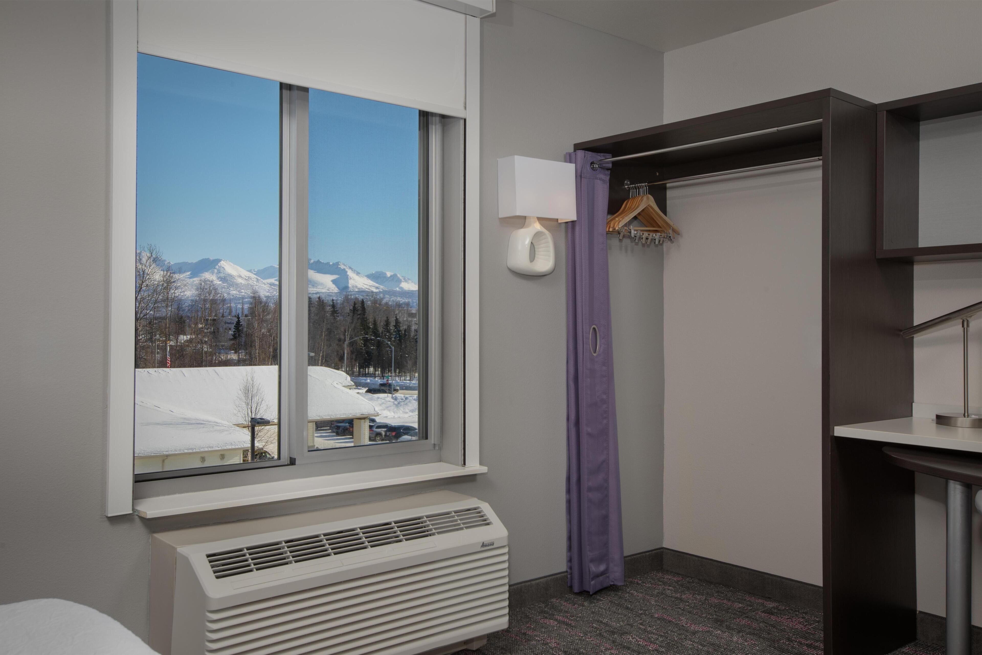 Une chambre d’hôtel avec une grande fenêtre, un radiateur, un rideau violet et une lampe fixée au mur.